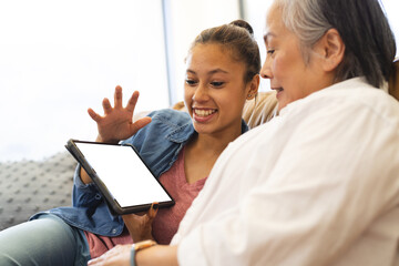 Asian grandmother with biracial teenage granddaughter at home, using tablet with copy space - Powered by Adobe