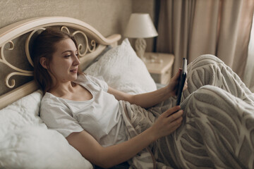 Young woman at home indoor lying on bed in bedroom with digital tablet