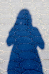 A womans shadow falls on the asphalt sidewalk in electric blue tint