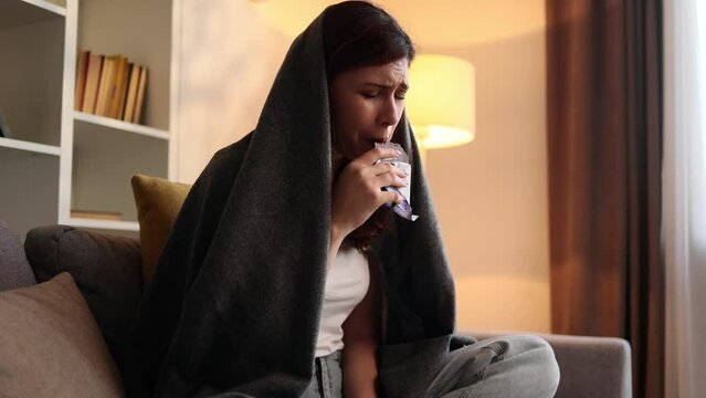 Portrait of sad young woman dealing with stress by eating food sitting on sofa at home Upset female wrapped in blanket crying and eating chocolate bar indoors alone Mental heath problem