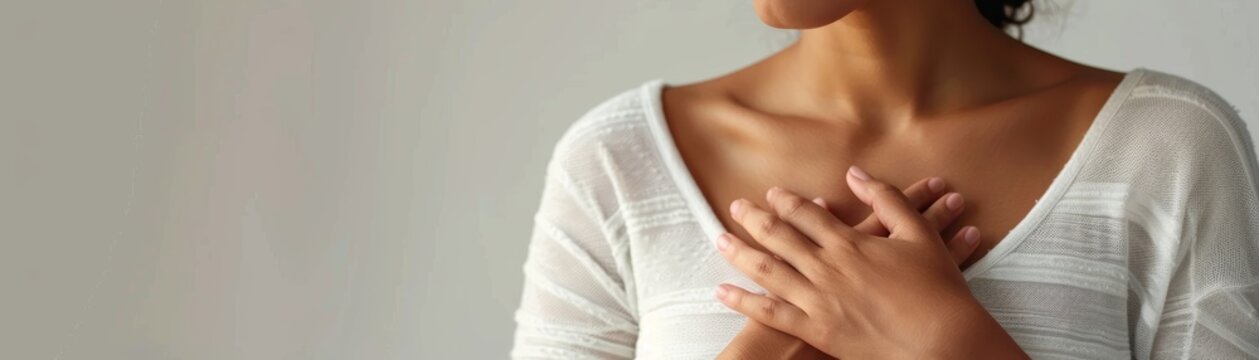 Close-up of a woman's hands placed over her heart, symbolizing gratitude, gratitude, well-being, and self-care, captured in a soft, warm light.