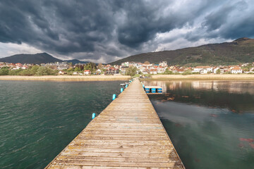 Naklejka premium Plav, Montenegro's serene lake offers a scenic backdrop for fishing at the old dock, with majestic mountains reflected in the calm waters.
