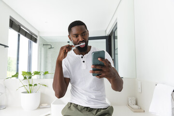 At home, African American man brushing teeth, checking phone