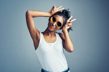 Studio, woman and funny with bunny ears, confidence and trendy accessory as sunglasses. Indian female model, peace sign and scream with emoji reaction, v symbol and girl by mockup in gray background