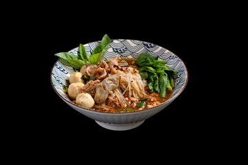 A bowl of Spicy Thai noodles soup with pork offal, meatballs and vegetables on black background