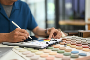 Cropped shot interior designer evaluating color swatches and using digital tablet at desk