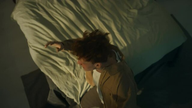 Top view of young Caucasian man falling on knees and shouting in rage and hopelessness at ceiling, feeling despair at night while alone at home