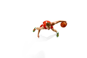 Aerial view of young athletic man, dressed red gear basketball player dribbling in motion against white studio background. Concept of professional sport, games, healthy lifestyle, tournament, action.