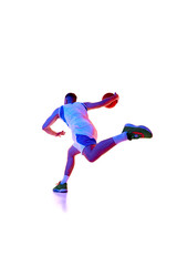 Low angle of young man dressed sportswear training dribbling technique in motion in neon light against white studio background. Concept of professional sport, games, healthy lifestyle, tournament.