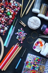 Colorful beads, coloring pencils, glitter, needles, string, hoop, tape and scissors on dark...