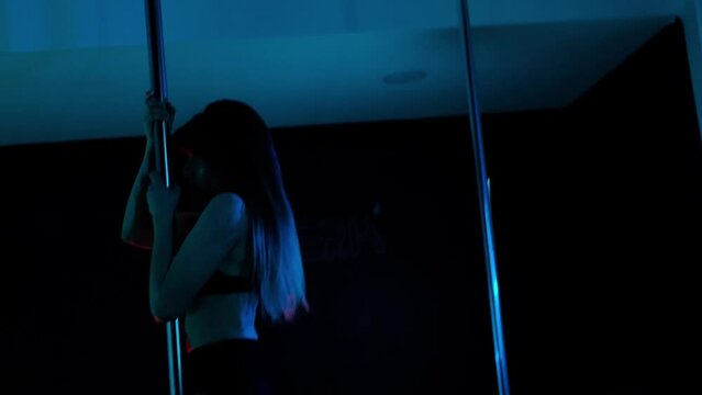 Young sexy pole dance woman. A girl in sexy black underwear and high-heeled platform shoes is dancing spinning on a pole in a dark studio with colorful bright lighting.