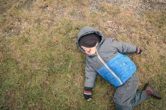 Top down view of little boy lying on grass in winter with cheeky smile