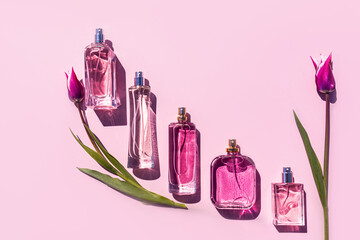 A set of perfume bottles of various shapes on a lilac background with delicate pink tulips. Flat...