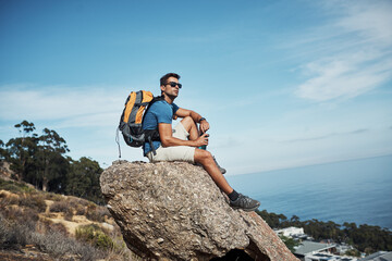 Man, forest and thinking with backpack on rock with view for calm, relax and serenity on adventure for solitude on mountain. Person, hiking and cliff outdoor with thoughts, peace and sustainability.