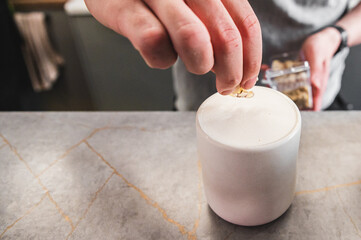 Hand barista sprinkling almond on a frothy beverage raf coffee in a white ceramic cup