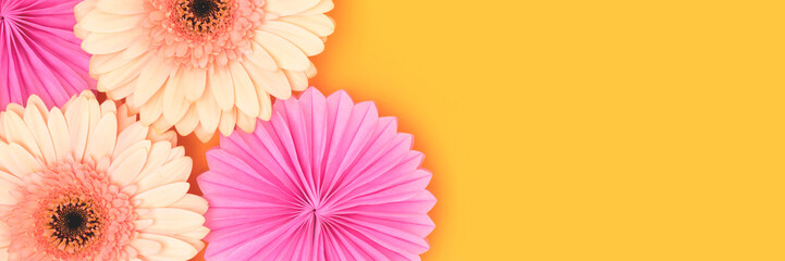 Banner with gerbera flowers and tissue paper fans on a yellow background.