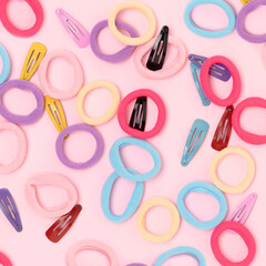 Many small multicolored hair scrunchies and clips on a pink background.