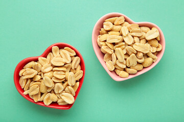 Peanuts in a heart shaped bowl on mint background.