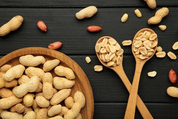 Fresh healthy peanuts in bowl and spoon on black wooden background.