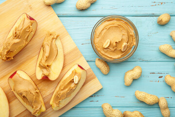 Slices of fresh apple with peanut butter and nuts on light blue wooden background.
