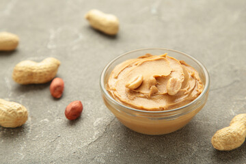 Bowl of peanut butter and peanuts on grey concrete background. Creamy peanut pasta in small bowl.