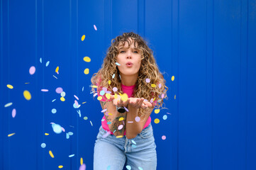 Carefree woman blowing confetti in front of blue wall