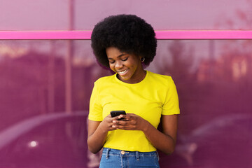 Smiling young Afro woman using smart phone in front of magenta window