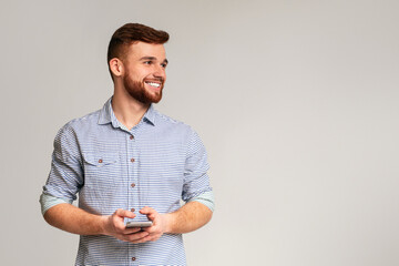 Young man blogger using his phone and looking away on copy space, isolated on grey studio background