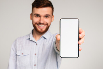 Young guy showing his phone with blank space on camera and smiling, isolated on grey studio background, mockup