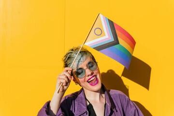 Happy lesbian woman holding rainbow flag in front of yellow wall