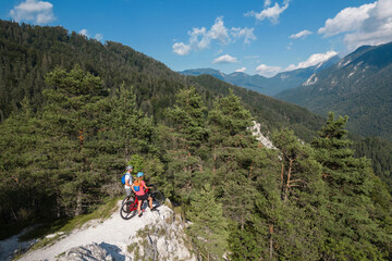 Fototapeta premium Two tourists cyclists on electric mountain bikes enjoying a beautiful highland landscape, aerial view.