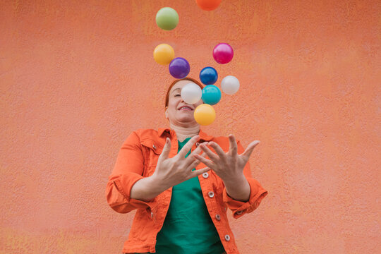 Mature woman juggling multicolored balls in front of orange wall