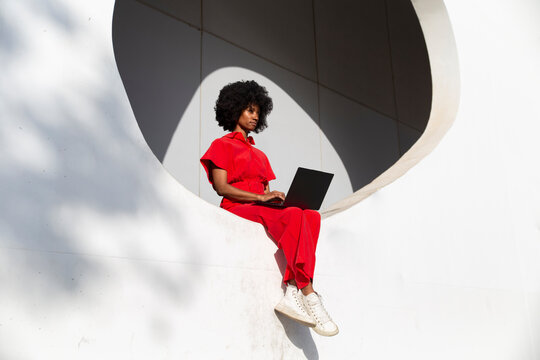 Mature woman in red jumpsuit sitting with laptop on white wall