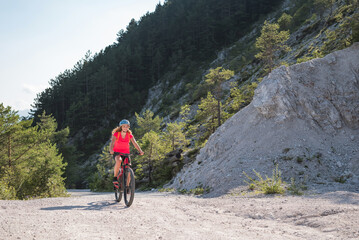 Female biker riding an electric mountain bike on a fine white stone trail, surrounded by fantastic...