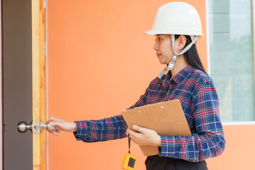 Asian woman home inspector in safety helmet holding clipboard, opening door. Depicts part of...
