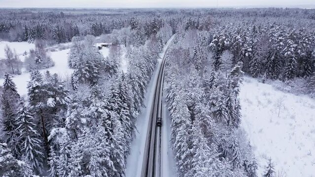 Aerial view in the estonian forest in winter avobe a road, everything is covered with snow, the drone flies over the pine trees capturing the snowy landscape, the road ann the cars.