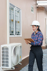 Asian female inspector in safety helmet holding clipboard, checking air conditioning unit. home...