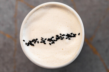 black sesame seeds on a frothy beverage raf coffee in a white ceramic cup