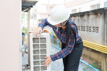 Asian female inspector in safety helmet checking outdoor air conditioning unit, ensuring proper...