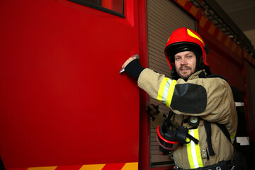 Portrait of firefighter in uniform near red fire truck at station