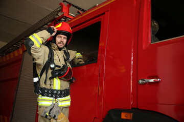 Fototapeta premium Portrait of firefighter in uniform near red fire truck at station