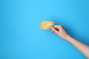 Woman holding credit card on light blue background, closeup. Space for text