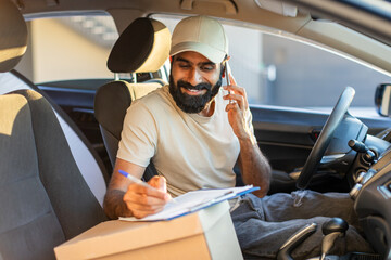 Indian delivery driver wearing a beige cap is seated inside his vehicle, talking on the phone and...