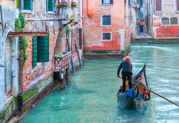 Venetian gondolier punting gondola through green canal waters of Venice Italy © muratart