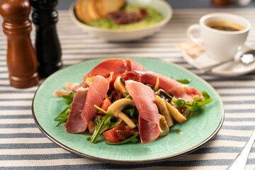 Bright salad with spinach, mushrooms, slices of prosciutto and tomatoes served on a white plate in...