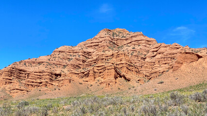 Fototapeta premium Large geological formations resulting from the weathering of rocks. Konorchek canyons in Kyrgyzstan. A red mountain against a blue sky. Trekking