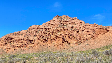 Large geological formations resulting from the weathering of rocks. Konorchek canyons in Kyrgyzstan. A red mountain against a blue sky. Trekking