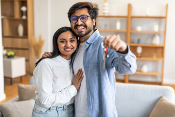 A joyful Indian couple embraces and smiles broadly while holding a set of keys, signifying the...