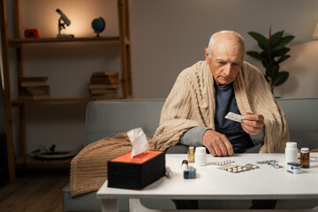 Sick man sitting on the sofa holding pills in his hands.