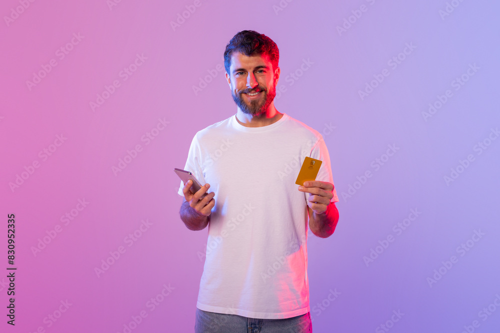 Poster A man is holding a card in one hand and a cell phone in the other. He appears to be focusing on the phone screen while holding the card. The background is neutral and nondescript.